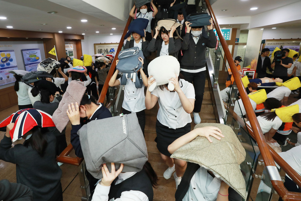 16일 오후 서울 동대문구 해성국제컨벤션고등학교에서 2018 재난대응 안전한국훈련의 일환으로 열린 국민 참여 지진 대피훈련에서 학생들이 머리를 보호한 채 대피하고 있다. 연합뉴스