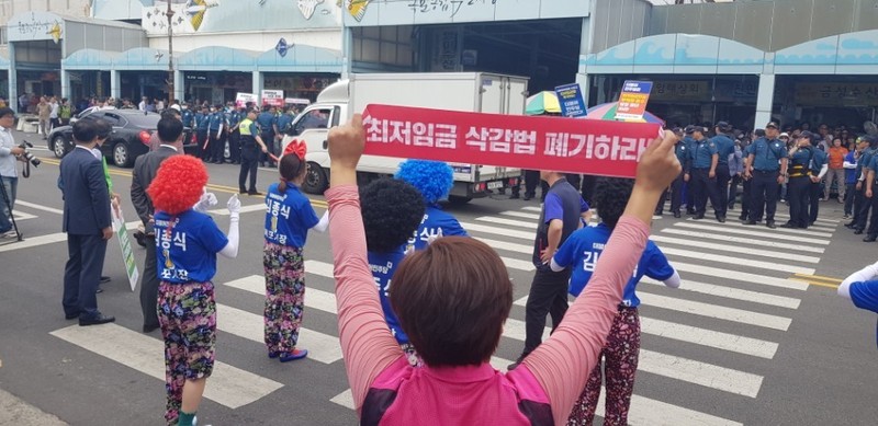 더불어민주당 중앙선대위원들이 전남 목포종합수산시장 유세에 나서기로 한 8일, 민주당 지도부가 도착하기 전 민주노총 전남본부 조합원들이 ‘최저임금 삭감법 폐기하라’ 등이 적힌 손팻말을 들고 시위를 펼치고 있다.