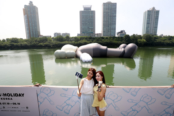 19일 오전 서울 송파구 잠실 석촌호수에서 모델들이 팝 아티스트 카우스의 공공 미술 프로젝트인 ‘‘카우스:홀리데이(HOLIDAY)‘‘를 배경으로 포즈를 취하고 있다. 연합뉴스
