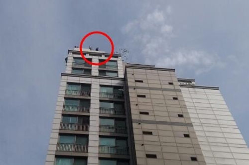 26일 서울 광진구 구의동의 한 20층짜리 주상복합단지 건물에서 중년남성(빨간 원 안쪽 모습)이 옥상에 올라가 기물을 부수며 소동을 부리고 있다. 이 남성은 옥상 바닥으로 추락해 의식불명 상태에 빠졌다. 독자 제공=연합뉴스