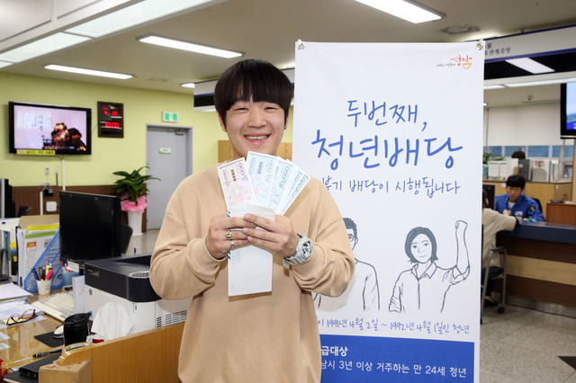 경기도가 광역 지방정부로는 처음으로 기본소득 성격의 청년배당금을 지급하기로 했다. 경기 성남시 한 주민센터에서 청년배당 명목의 지역화폐를 받아든 청년이 환하게 웃고 있다. 성남시 제공