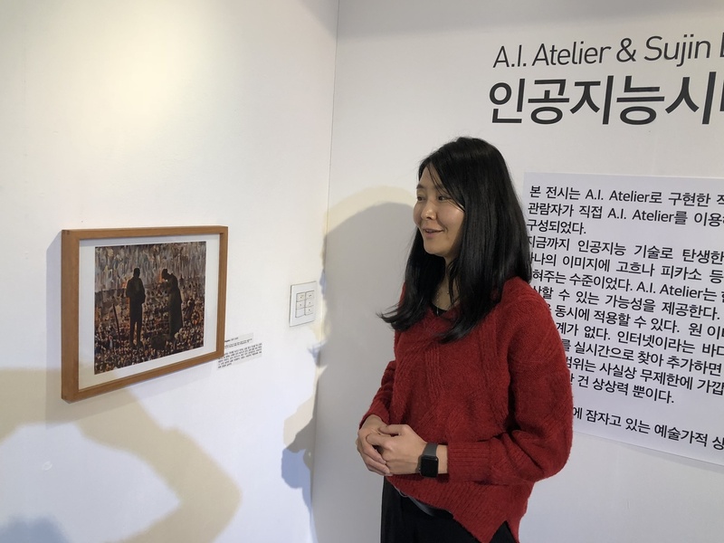 ‘인공지능시대의 예술작품’ 전시회에서 이수진 작가가 A.I. 아틀리에와 협업해 밀레의 ‘저녁종’을 모티브로 창작한 작품을 설명하고 있다. 이 작가는 여자의 발 밑에 놓인 감자바구니가 아이의 관이었다는 이야기에 영감을 받아, 프랑스 혁명 당시 봉기한 민중의 이미지를 A.I. 아틀리에로 합성해 작품으로 표현했다.