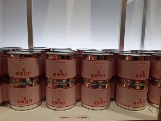 ‘메이드 인 조선’ 전시 말미 아트숍에서 팔고있는 ‘불알캔디’통. ‘불알’은 북한에서 전구를 부르는 순우리말이다. 라벨의 글자와 이미지는 북한풍이지만, 여러개의 캔디통을 늘어놓은 모양새는 앤디 워홀의 팝아트 작품인 캠벨수프깡통들을 쌓은 모습을 떠올리게 한다.