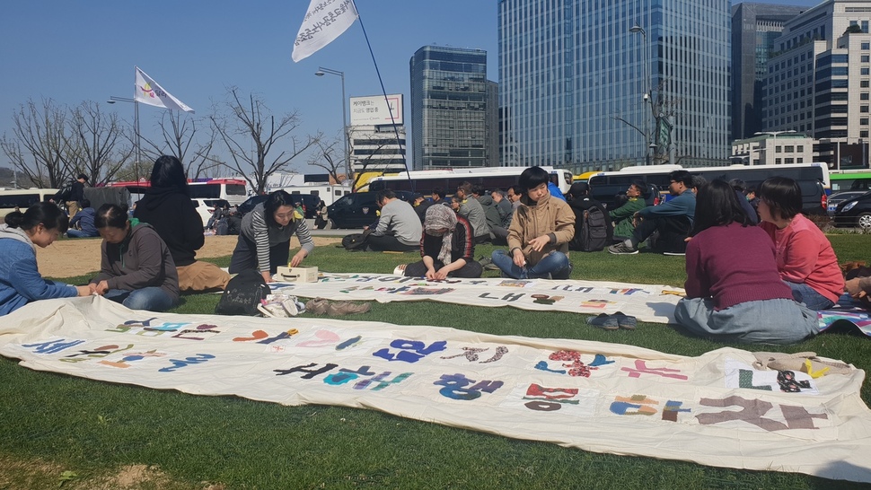 13일 서울 종로구 광화문광장에서 ‘뜨개x바느질 행동단’이 참사를 추모하는 천 펼침막을 만들고 있다. 오연서 기자