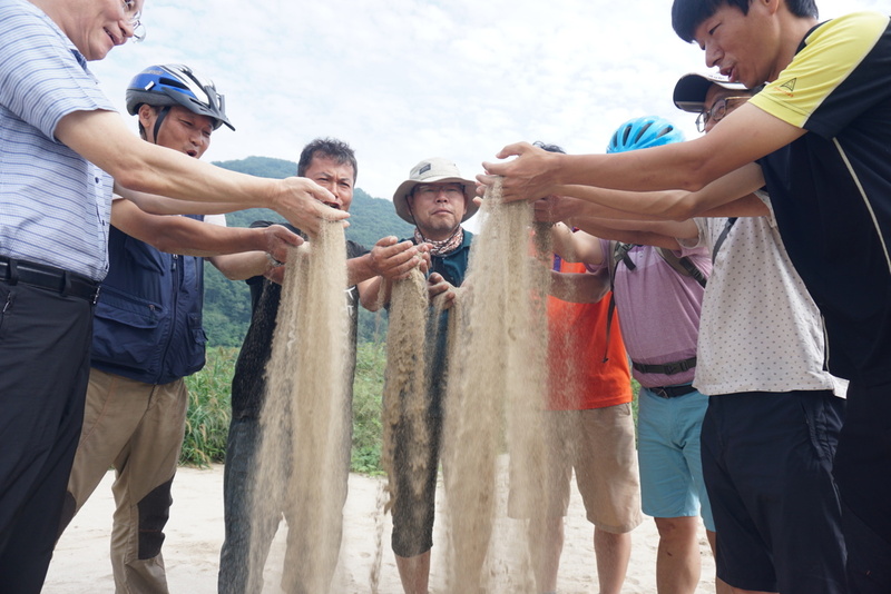 지난 23일 ‘자전거 탄 금강’ 참가자들이 손으로 충남 공주 고마나루 모래톱의 모래를 퍼 올려 흩뿌리고 있다.