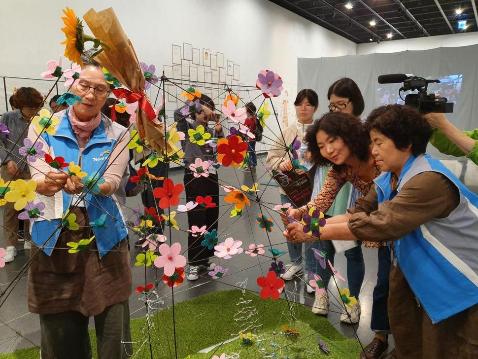 지난 21일 연세대 백양누리 무악로터리홀에서 열린 ‘밀양 할매 그리고 말하다’ 전시회에서 여성주의 현대화가 이충열(오른쪽 둘째)씨가 밀양 용회마을 구미현 할머니(맨 왼쪽), 김옥희 할머니(맨 오른쪽)와 함께 쓰러진 송전탑 조형물에 꽃을 만들어 매달고 있다. 이지은 기자